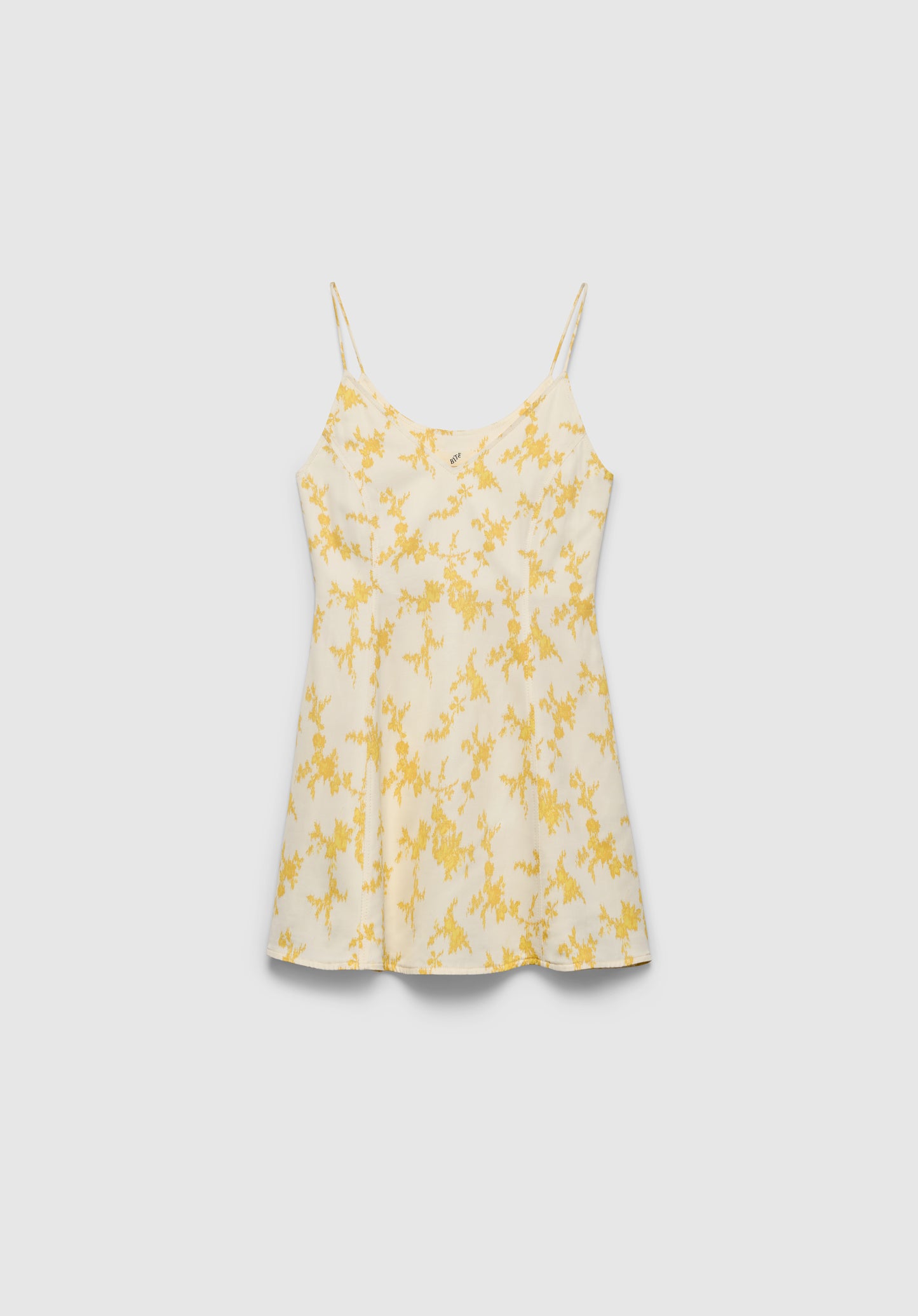 A cream-colored slip dress with thin spaghetti straps and a soft flared silhouette, featuring a delicate yellow floral print, displayed against a plain background.
