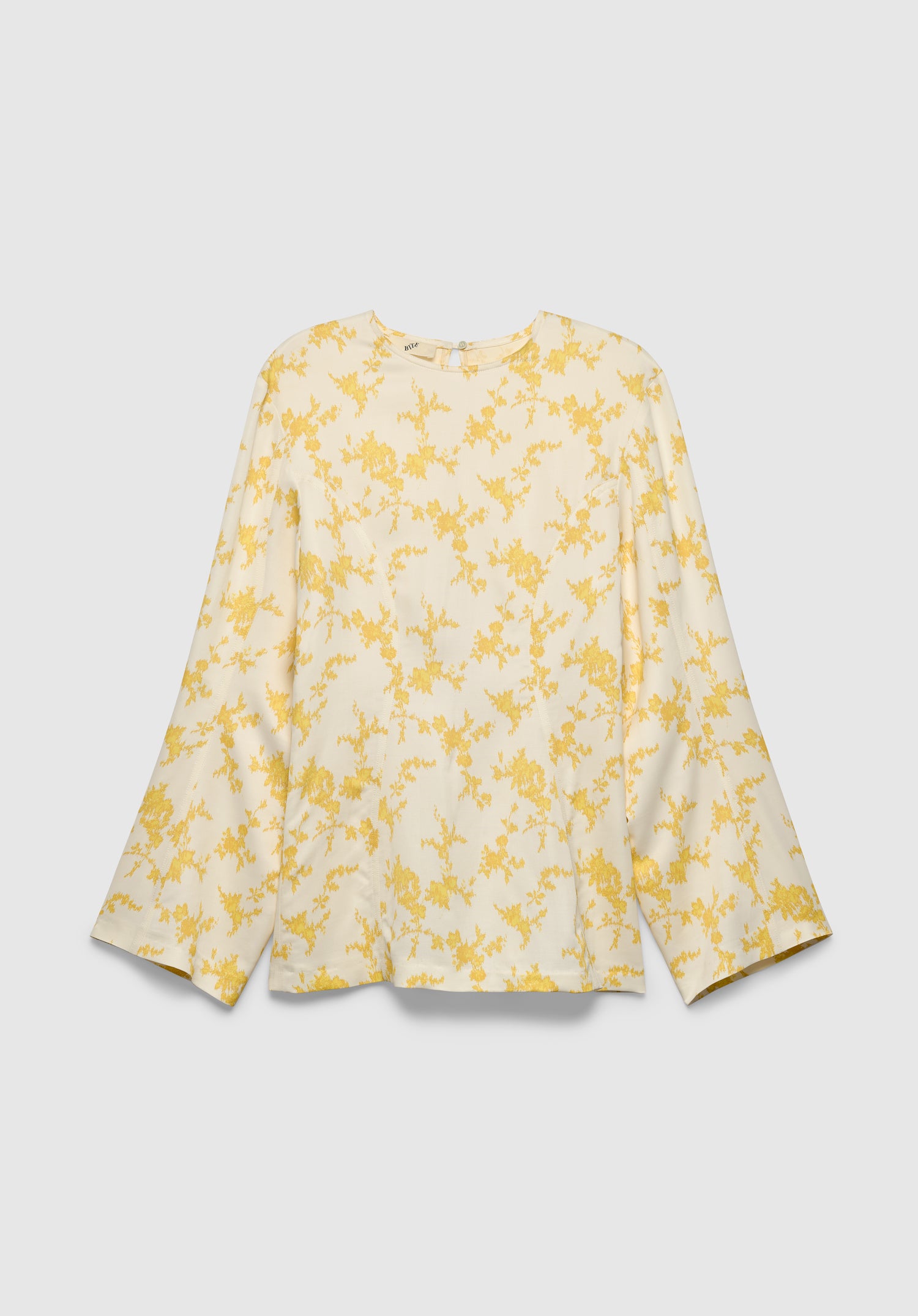 A cream-colored long-sleeve blouse with a relaxed fit, featuring a round neckline and a delicate yellow floral print, displayed against a plain background.
