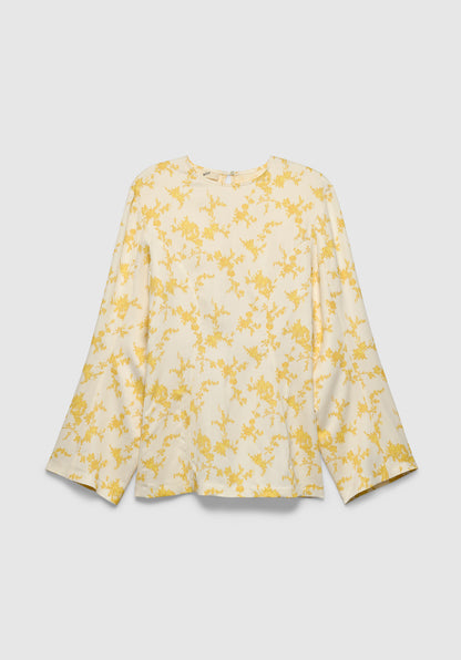 A cream-colored long-sleeve blouse with a relaxed fit, featuring a round neckline and a delicate yellow floral print, displayed against a plain background.
