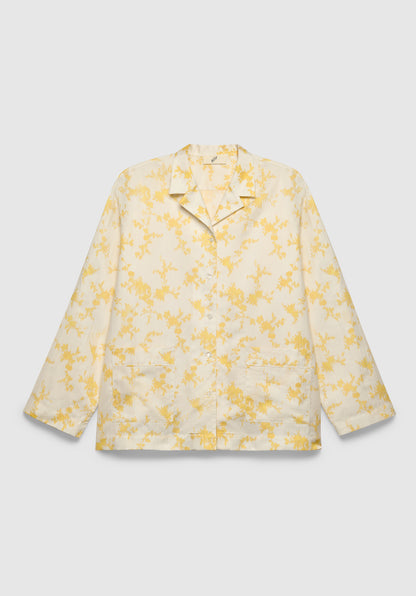 A cream-colored long-sleeve shirt with a relaxed fit, featuring a notched collar, front button closure, patch pockets, and a delicate yellow floral print, displayed against a plain background.

