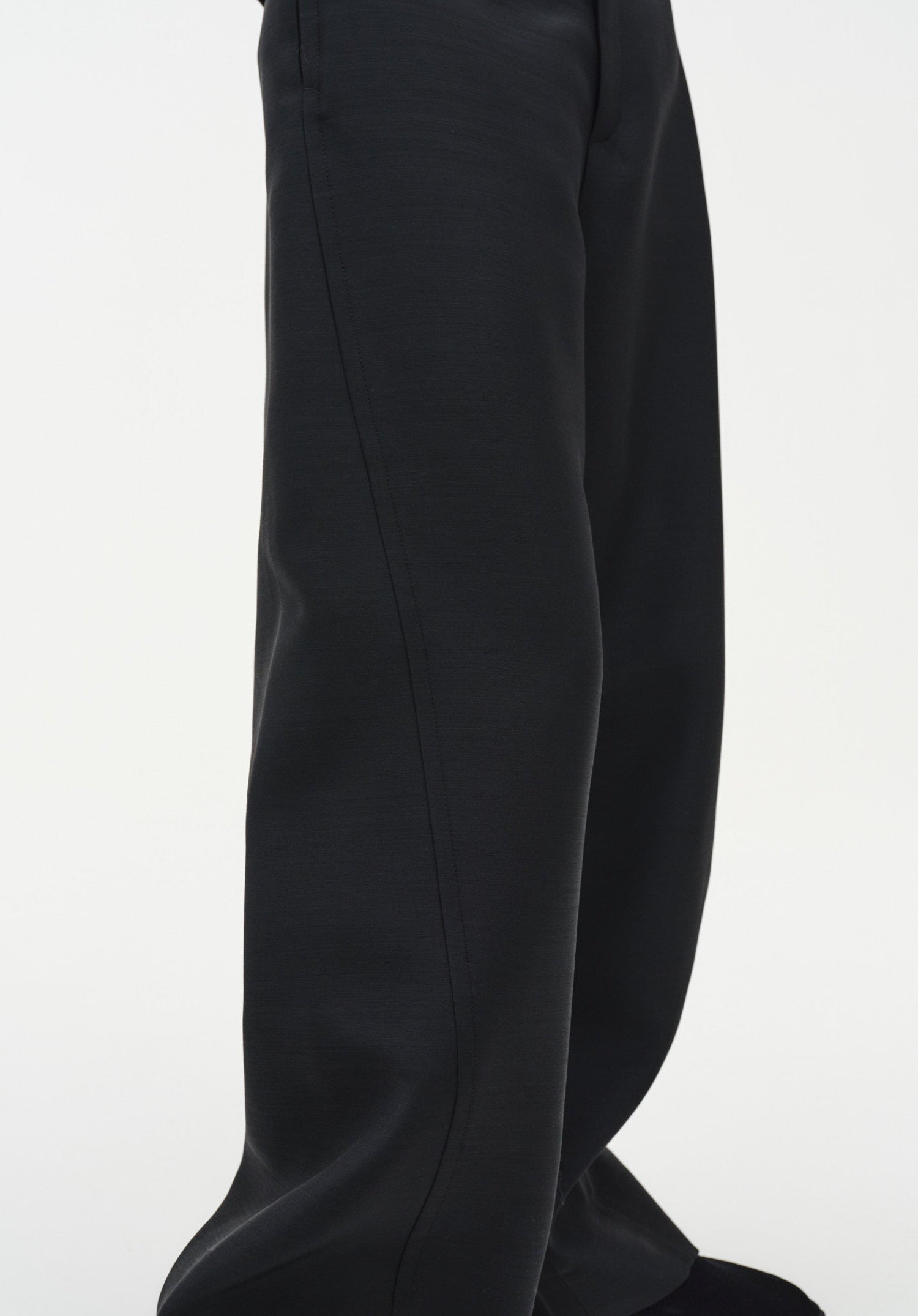 Close-up of black wide-leg trousers highlighting the smooth fabric and a vertical seam running down the leg, showing a clean, structured drape.
