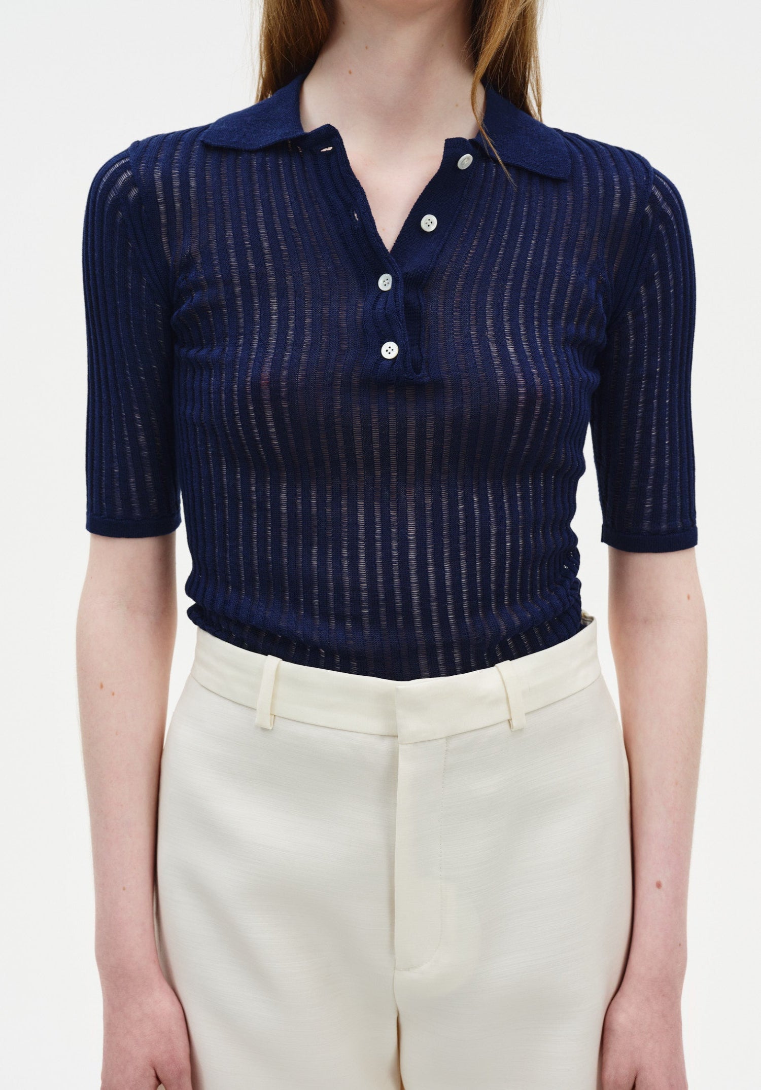 A close-up front view of a woman’s torso, showing a relaxed upright posture with her arms at her sides against a plain background.
