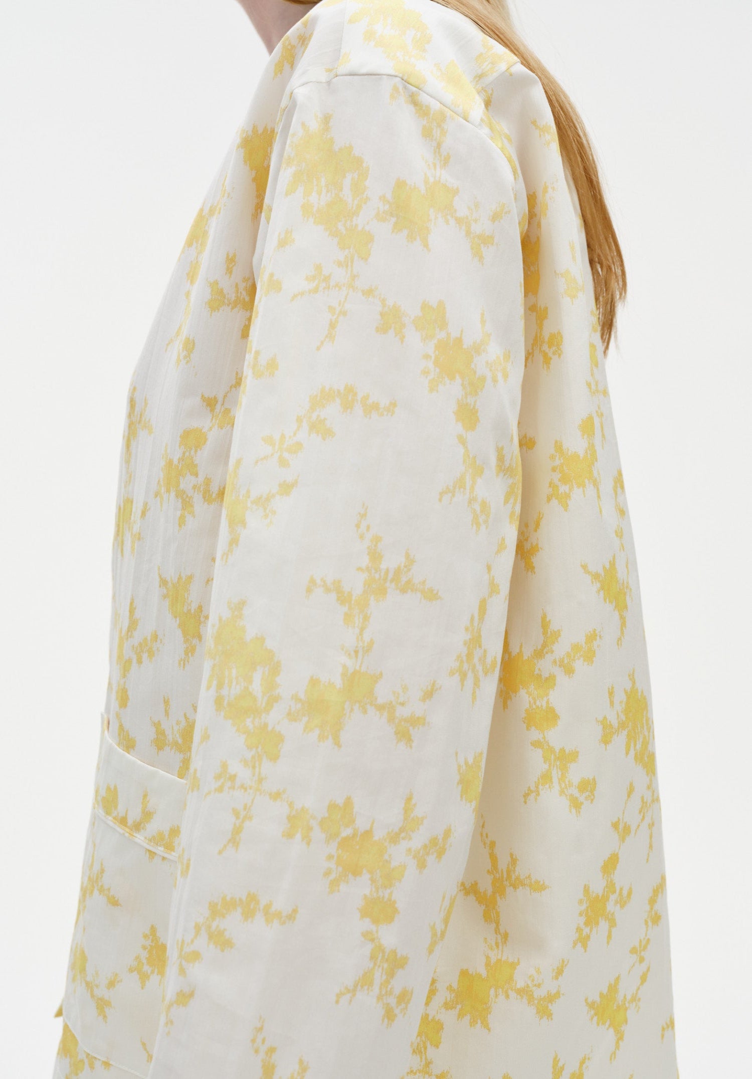 Close-up side view of a white long-sleeve top with a soft yellow floral pattern, highlighting the relaxed fit, smooth fabric, and subtle drape along the arm and shoulder.
