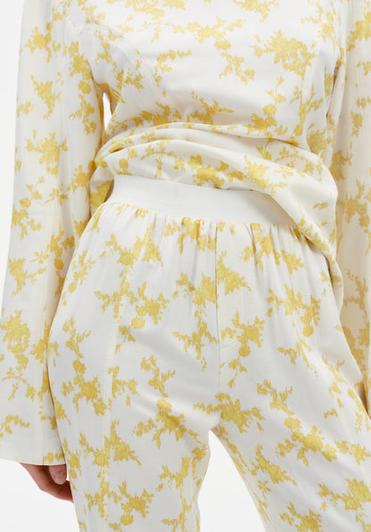 Close-up of cream trousers with a yellow abstract floral print, featuring a high elasticated waistband and soft draping fabric, paired with a matching long-sleeve top.
