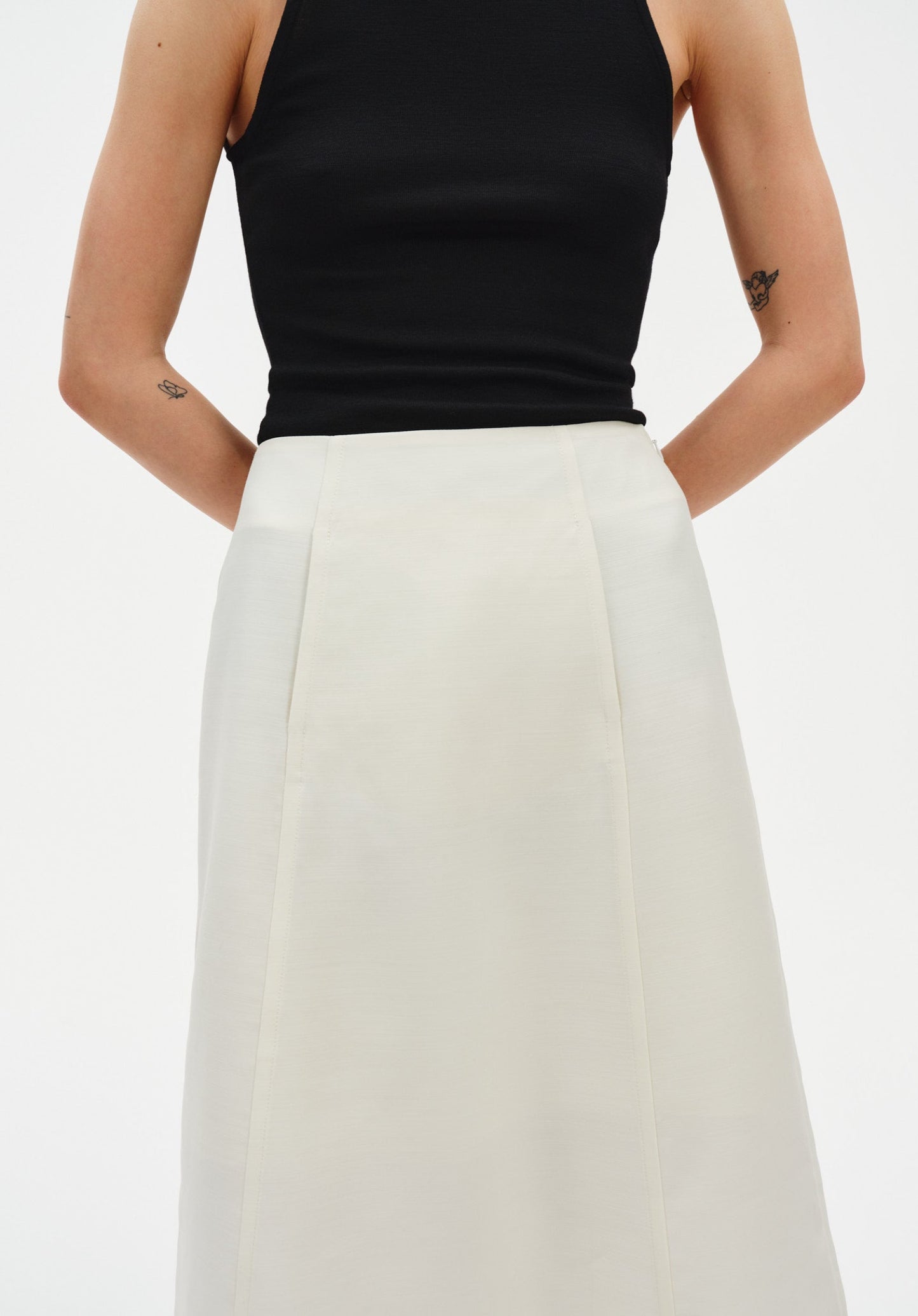 Close-up of a black sleeveless top tucked into a cream-colored midi skirt, highlighting the smooth, fitted fabric and clean seam detailing at the waist.

